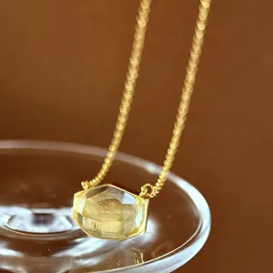 Macro detail of a minimalist irregular cut yellow crystal pendant with a gold chain.