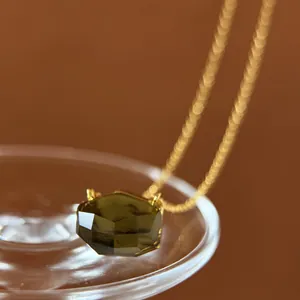 Close-up of minimalist gold necklace with irregular cut olive green crystal pendant