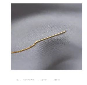 Detailed macro shot of a delicate gold threader earring on soft grey fabric background.