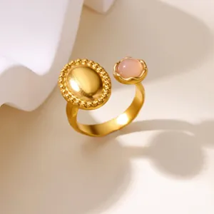 Close-up view of a gold-tone stainless steel open ring with a pink stone and oval detail.