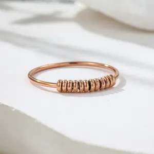 Nahaufnahme eines roségoldenen Anti-Angst-Rings mit zehn beweglichen Perlen auf weißem Stein.