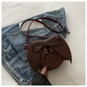 Brown bat wing shaped crossbody bag with lace-up detail on denim backdrop