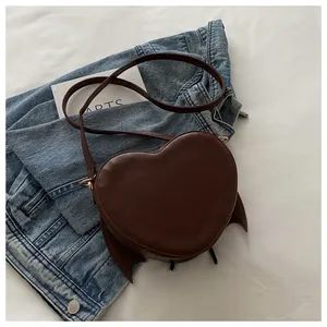 Close-up view of quirky brown heart-shaped bag with bat wings on denim background