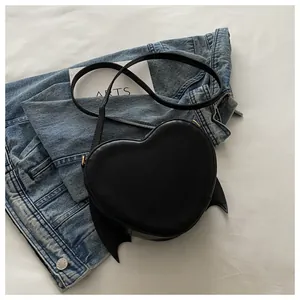 Black heart-shaped crossbody bag with bat wing details and golden hardware accent.