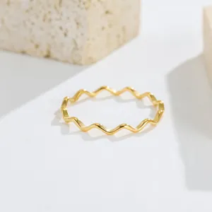 Macro view of a minimalist gold wave-pattern stainless steel ring on a white surface.