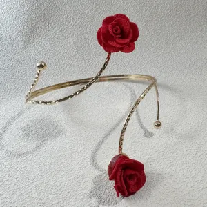 Detaillierte Ansicht eines goldenen Spiral-Armreifs mit eleganten roten Stoffrosenblüten.