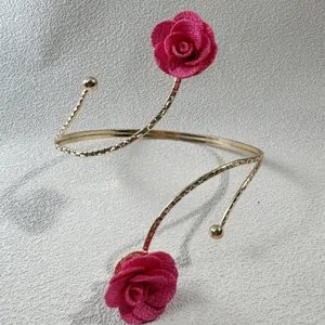 Detail eines eleganten goldenen Armreifs mit zwei pinkfarbenen Stoffrosen und Struktur.