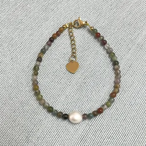 Gros plan d'un bracelet en pierres multicolores avec une perle d'eau douce naturelle.