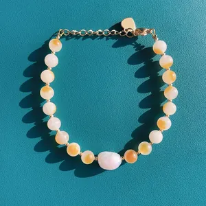 Gros plan d'un bracelet en perles de pierre jaune et perle baroque sur fond turquoise