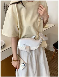 Süße silberne Umhängetasche in Walform, getragen von einem Model im cremefarbenen Outfit