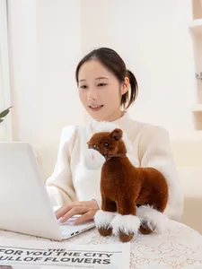 Realistic brown plush horse toy with white fluffy mane standing on a table by laptop