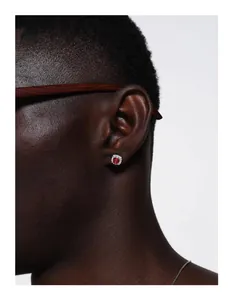 Close-up of a silver iced-out stud earring with a red stone on a male model's ear lobe.