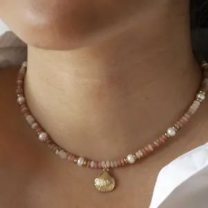 Detail of a beaded necklace with pink stones, pearls, and a golden shell pendant.