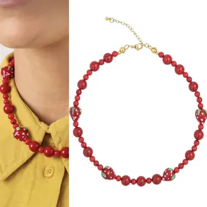 Vue côte à côte d'un collier de fraises rouges sur un modèle et à plat.