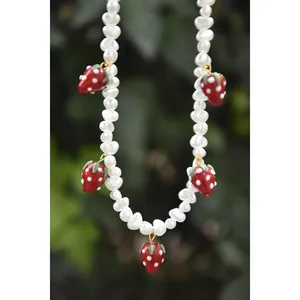 Gros plan d'un collier en perles d'eau douce avec des breloques fraises rouges de détail