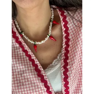 Détail d'un collier de perles d'eau douce avec breloques piment en verre sur modèle.