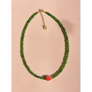 Gros plan d'un collier de perles vertes avec un charmant détail de fraise en verre