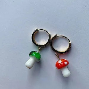 Vue détaillée de boucles d'oreilles créoles avec breloques champignons en verre rouge et vert