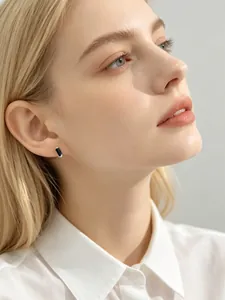 Close-up of minimalist black square zircon stud earring worn by a model in a white shirt