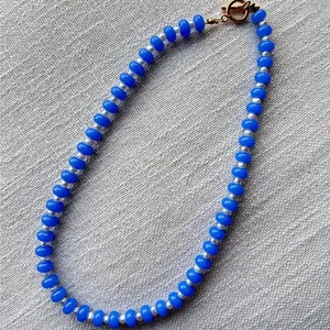 Detalle de cuentas de ábaco azules y perlas blancas sobre un fondo de tela texturizada.
