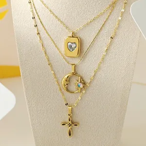 Detailed close-up of gold-tone layered necklace with heart, moon, and cross pendants