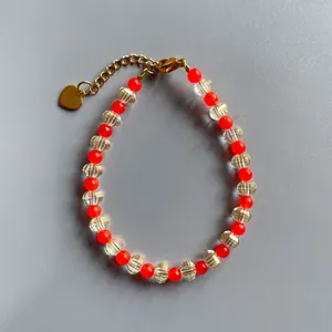 Détail d'un bracelet de perles colorées avec un charm en cœur doré et un fermoir mousqueton.