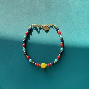 Détail d'un bracelet en perles de pierres naturelles colorées avec un charme de cœur doré