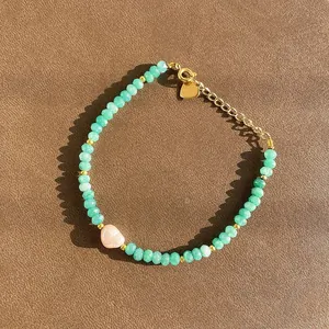 Détail d'un bracelet en pierre naturelle verte avec une perle rose sous un soleil éclatant.