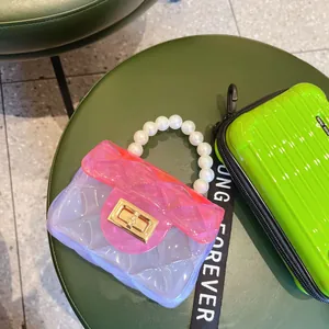 Primo piano di una mini borsa jelly in PVC trasparente con manico di perle e oro.