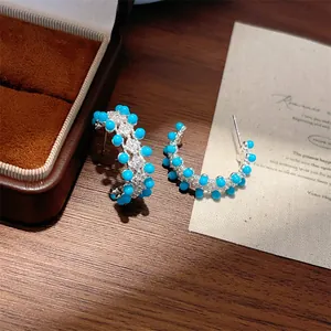 Detailopname van elegante turquoise en kristallen oorringen op houten tafel.