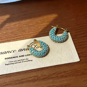 Detailweergave van elegante gouden creolen ingelegd met levendige blauwe turkooisstenen.