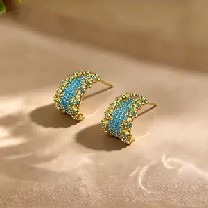 Gedetailleerde macro-opname van vergulde oorringen met kleine turquoise steentjes.