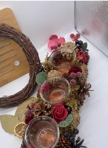 Detail view of a rustic Christmas wreath candle holder with pine cones and red roses