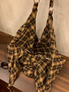 Gros plan d'un grand sac hobo en toile à carreaux rétro posé sur un bureau en bois