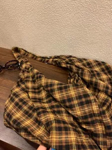 Détail d'un sac hobo en toile à carreaux vintage sur une surface en bois brun.