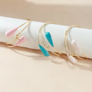 Bracelets de bras dorés élégants avec breloques gouttes d'eau colorées sur fond beige.