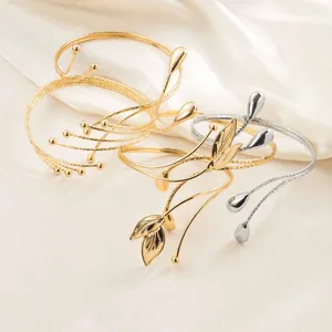 Détail de bracelets de bras ouverts dorés et argentés aux motifs géométriques de feuilles.