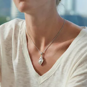 Close-up of a silver conch shell pendant necklace worn by a model in natural light.