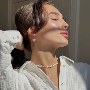 Elegant handmade shell heart beaded necklace and earrings on model in warm sunlight.