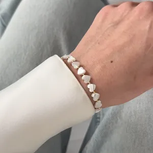 Close-up of handmade white shell heart beaded bracelet with gold accents on wrist