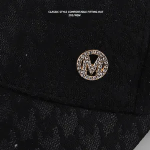 Close-up van zwarte kant baseballpet met glinsterende strass M-logo badge detail