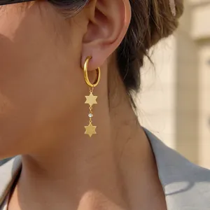 Close-up detail of golden stainless steel star dangle hoop earrings with small crystal accent.
