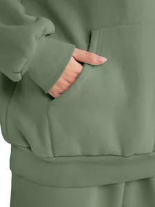 Detail view of sage green hoodie showing kangaroo pocket and ribbed cuff texture.