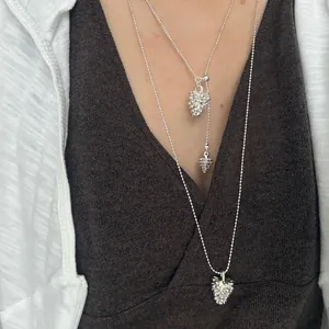 Primer plano de collares con colgante de piña plateados sobre un vestido gris con cuello en V