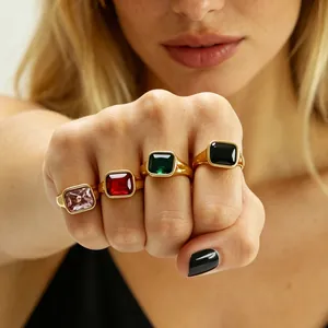 Detail of four elegant square zirconia rings in pink red green and black on female fingers