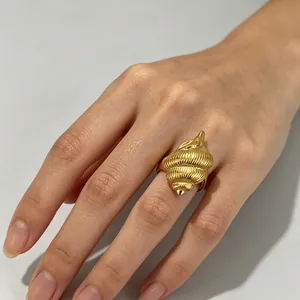 Primo piano di un anello a conchiglia dorato indossato, con dettagli marini raffinati.