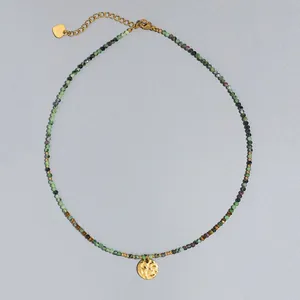 Detalle de un collar de piedras naturales con un colgante martillado dorado fino.