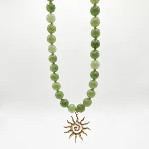 Detalle de un collar vintage de piedras naturales verdes con un colgante de sol dorado.