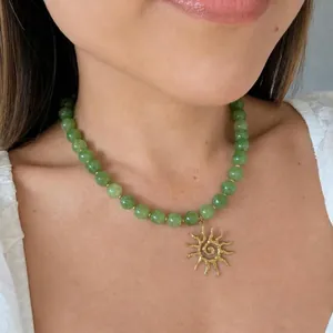 Detalle de collar de piedra natural verde con colgante de sol dorado en modelo