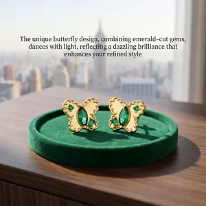 Close-up of gold butterfly earrings with green emerald-cut gemstones on a green velvet tray